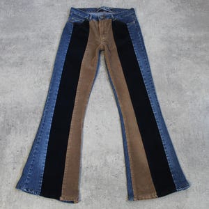 Op de afbeelding: Een paar blauwe denim broek met wijde pijpen en bruine en zwarte corduroy panelen langs de benen.