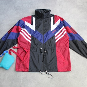 Puede incluir: Una chaqueta cortavientos negra, roja y azul con rayas blancas y la palabra "adidas" en la parte delantera.