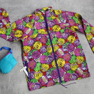 May include: A colorful, lightweight jacket with a zipper closure. The jacket is covered in a pattern of colorful circles with numbers and letters printed on them. The jacket is made of a water-resistant material.