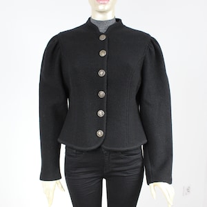 May include: A black wool jacket with a stand-up collar and button closure. The jacket has a fitted silhouette and long sleeves.