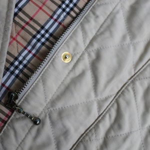 May include: A beige quilted jacket with a zipper closure and a Burberry check lining. The jacket has a gold zipper pull and a gold button.
