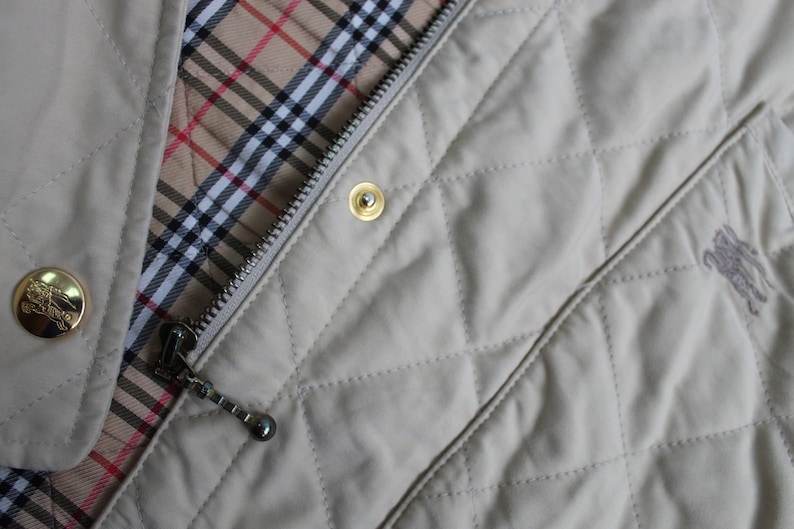 May include: A beige quilted jacket with a zipper closure and a Burberry check lining. The jacket has a gold zipper pull and a gold button.