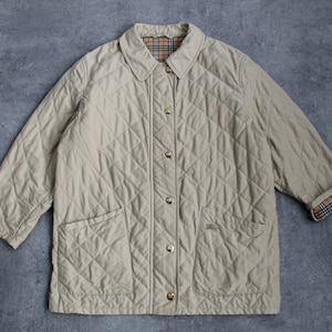 May include: A beige quilted jacket with a button-up front and two pockets. The jacket has a plaid lining visible at the collar and cuffs.