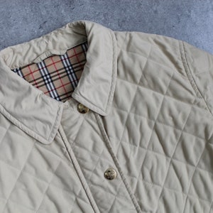 May include: A beige quilted jacket with a plaid lining and gold buttons. The jacket has a classic design and is perfect for layering in cooler weather.