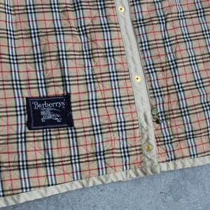 May include: A beige quilted jacket with a black and red plaid pattern. The jacket has a zipper closure and a Burberrys label on the left side.