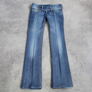 Può includere: Jeans blu in denim con design a zampa d'elefante. I jeans hanno una chiusura a doppio bottone e un effetto lavato sbiadito. Il capo è steso su una superficie grigia.