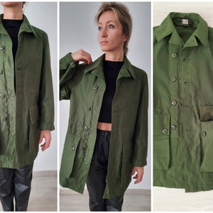 May include: A green utility jacket with a button-up front, two large pockets on the front, and a smaller pocket on the right side. The jacket has a collar and long sleeves.