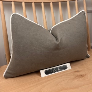 May include: A gray linen pillow with a white piping detail. The pillow is sitting on a wooden chair.