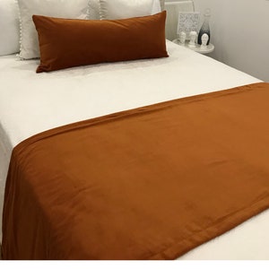 Könnte beinhalten: Ein weißes Bett mit einer braunen Samtdecke und einem braunen Samtkissen. Das Bett hat weiße Kissen und eine weiße Bettdecke.