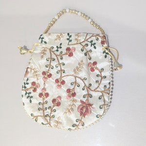 May include: A white drawstring bag with a floral embroidery design. The bag has a beaded handle and a tassel.