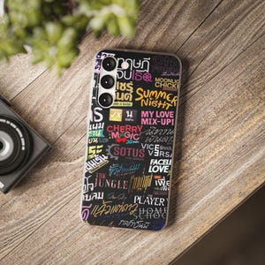 Op de afbeelding: Een zwarte telefoonhoes met een witte rand. De hoes is bedekt met kleurrijke tekst en afbeeldingen, waaronder de woorden "Summer Night", "My Love", "Cherry Magic", "Sotus", "The Jungle", "Player" en "Home School".