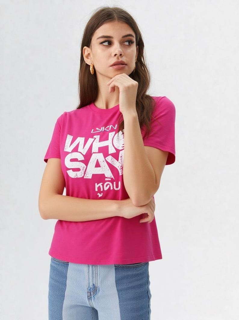 May include: A magenta t-shirt with white text that reads "WHO SAY" in a bold, stylized font. Below the English text is text in a different language. The model is wearing blue jeans.