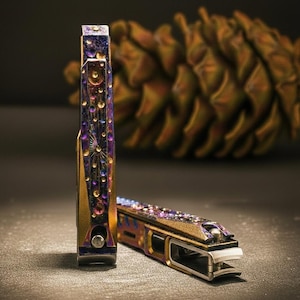 May include: Two decorative nail clippers with a gold and iridescent finish. The clippers feature a pattern of purple, gold, and blue detailing. One clipper is upright, the other is lying down.