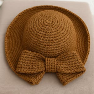 Könnte beinhalten: Ein brauner gehäkelter Sonnenhut mit einer großen braunen gehäkelten Schleife.