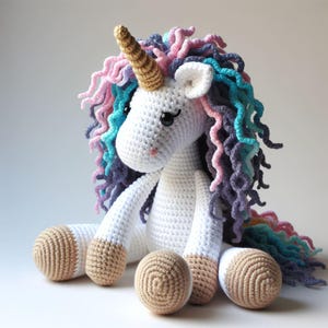 Può includere: Un unicorno bianco all'uncinetto con un corno dorato e una criniera arcobaleno. L'unicorno è seduto con le gambe incrociate e ha zoccoli marroni all'uncinetto.