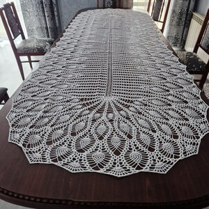 Könnte beinhalten: Weißer gehäkelter Tischläufer mit einem zarten, filigranen Design. Der Läufer hat einen gewellten Rand und ein sich wiederholendes Muster aus kleinen Kreisen und Schlaufen.