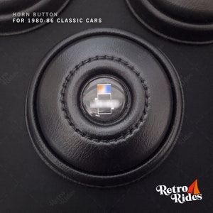 Könnte beinhalten: Schwarzer Leder-Hupe-Knopf mit einem transparenten Kunststoff-Knopf-Einsatz. Der Knopf-Einsatz hat ein blaues und orangefarbenes Design. Der Text "HORN BUTTON FOR 1980-86 CLASSIC CARS" ist über dem Knopf gedruckt.