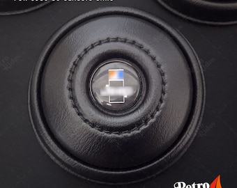 May include: Black leather horn button with a clear plastic button insert. The button insert has a blue and orange design. The text "HORN BUTTON FOR 1980-86 CLASSIC CARS" is printed above the button.