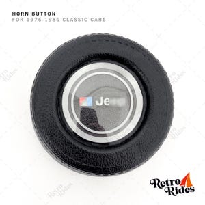 Op de afbeelding: Zwarte ronde claxonknop met een zilveren rand en een doorzichtige plastic afdekking. De knop heeft een Jeep-logo met de tekst "Jeep" in de afdekking.