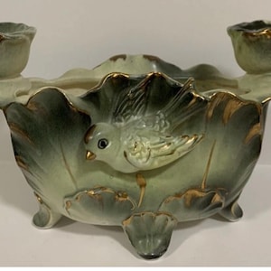 May include: A vintage ceramic centerpiece with a bird and leaf design. The light green and gold-trimmed bowl has two candle holders. The bird is light green with gold accents. The bowl is supported by three small feet.
