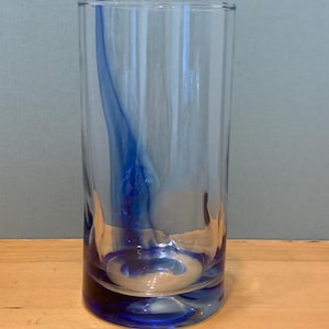 Peut inclure: Un grand verre transparent avec un motif tourbillonnant bleu vif. La base et l'intérieur du verre présentent une teinte bleu foncé, créant un contraste saisissant. Le verre est cylindrique et semble être fait d'un matériau lisse.