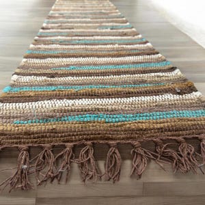 May include: A woven rug with brown, beige and turquoise stripes. The rug has a fringe on both ends.