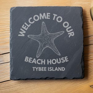 May include: Black slate welcome sign with white text that reads "Welcome to our Beach House Tybee Island". A white starfish is in the center of the sign.