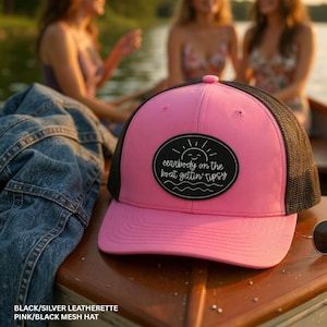 May include: A pink and black mesh hat with the text "eenrbody on the boat gettin' tipsy" on a black oval patch. The hat has a pink front and a black mesh back. The hat is made of leatherette.