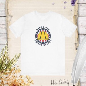 May include: White t-shirt with a blue and red circle design featuring a yellow hard hat and the text "Labor Day United States".