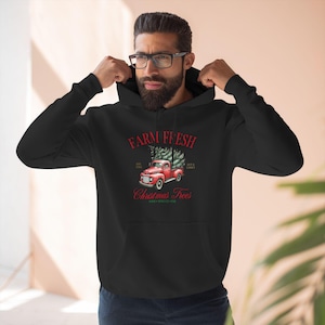Puede incluir: Sudadera negra con un camión rojo que lleva un árbol de Navidad y el texto "Farm Fresh Christmas Trees" en rojo.