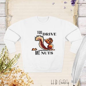 Puede incluir: Sudadera blanca con una ardilla que lleva nueces y el texto "You drive me nuts".