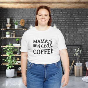 May include: White t-shirt with black text that reads "Mama's needs coffee" and a small coffee cup icon.