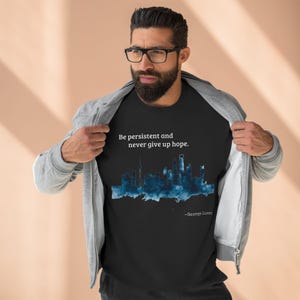 May include: Black t-shirt featuring a blue cityscape graphic and the quote "Be persistent and never give up hope." by George Lucas.