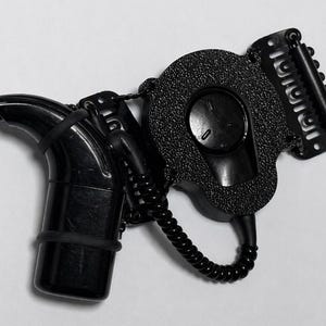 May include: A black hair styling tool with a curved nozzle, a textured circular component, and a clip. The tool has a coiled cord and a button on the circular component. The design is sleek and modern.