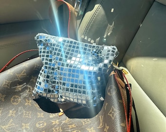 Può includere: Una borsa rettangolare ricoperta da piccole tessere a specchio argentate e riflettenti che creano un effetto palla da discoteca. La borsa presenta una forma strutturata con una lucentezza metallica, riflette luce brillante sulla superficie e include una tracolla sottile.