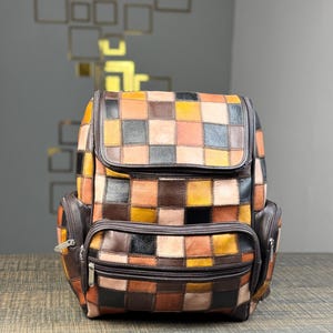 May include: A brown leather backpack with a patchwork design of different colored squares. The backpack has multiple pockets and zippers.