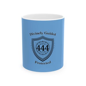 May include: A light blue ceramic mug with a white interior. The mug features the text "Divinely Guided Protected" and a shield design with the number "444" in the center.