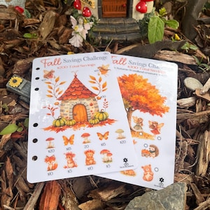 May include: Two Fall Savings Challenge sheets with illustrations of autumn themes, including a house, pumpkins, and woodland creatures. The sheets have various amounts listed, such as $5, $10, $15, and $20. A miniature mushroom house is in the background.