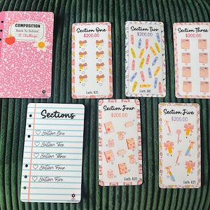 May include: A collection of pink and white stationery items, including a notebook and several cards with various designs and text. The notebook reads "COMPOSITION Back To School 15 Challenge". The cards have illustrations of school supplies.