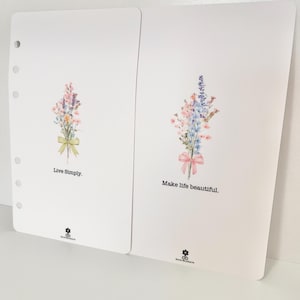 May include: Two white cards with floral illustrations and inspirational quotes. The left card features a bouquet of pink and blue flowers with a yellow ribbon and the text "Live Simply." The right card features a bouquet of pink and blue flowers with a pink ribbon and the text "Make life beautiful."
