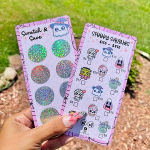May include: Two pink Halloween-themed scratch-off cards. One says "Scratch & Save" with a ghost graphic. The other says "Spooky Savings" with various Halloween character graphics and dollar amounts.