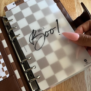 May include: A translucent plastic planner divider with a brown and white checkered pattern. The text "BILLS... Boo!" is printed in black script in the center. A small "db DAISYBUDGETS" logo with a flower icon is in the bottom right corner.