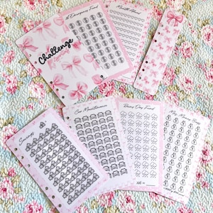 May include: A collection of pink and white budgeting challenge inserts. The inserts feature illustrations of bows, houses, cars, rain clouds, and money bags. Text includes "Challenge Essentials", "Emergency Fund", "Month Ahead", "Savings", "Car Maintenance", "Rainy Day Fund", and "Mrs. Money Bags".