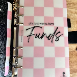 May include: A translucent plastic planner divider featuring a pink and white checkered pattern. The text reads "girls just wanna have Funds" in black script and print. A "HIGH PRIORITY" tab extends from the top, and a gold chain is attached.