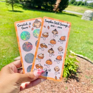 May include: Two rectangular cards with an orange border are held up. One card says "Scratch & Save" and has three scratch-off circles. The other card says "Pumpkin Patch Savings" and has illustrations of pumpkins, turkeys, and desserts.