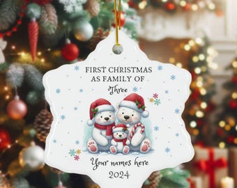 May include: A white ceramic Christmas ornament in a snowflake shape. It features a watercolor illustration of three polar bears wearing Santa hats and scarves. Text reads "First Christmas as Family of Three" and "Your names here 2024".