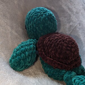 May include: A crocheted plush toy turtle with a dark brown shell and teal green limbs and head.