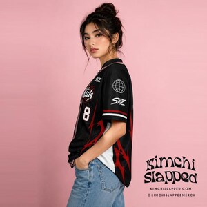 May include: A black short-sleeved button-down jersey featuring red flame-like patterns, the number 8, and the text SKZ on the front. The sleeve displays a globe icon and the text SKZ. The jersey has white side panels and a black collar.