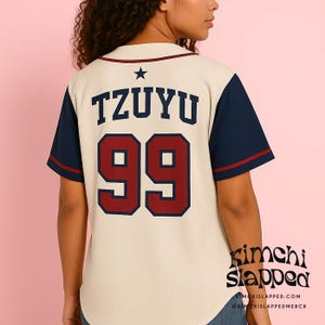 May include: Cream-colored baseball jersey with navy blue sleeves and red trim. The back features the name "TZUYU" above the number "99" in a bold, red font. A black star is above the name. The jersey has a classic, sporty design.