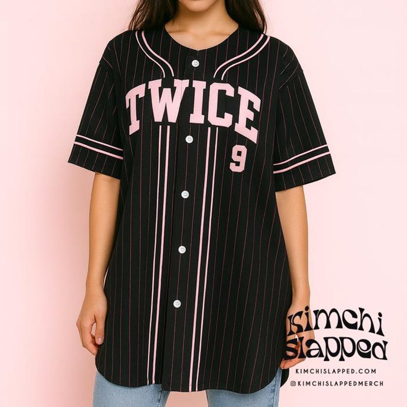 Pode incluir: Camisola de baseball preta com riscas rosa, com a palavra "TWICE" em letras rosa e o n&uacute;mero "9". A camisola tem uma frente abotoada e acabamentos brancos. O log&oacute;tipo Kimchi Slapped &eacute; vis&iacute;vel no canto inferior direito.